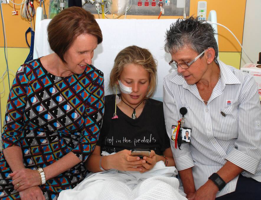 Staying in touch: Patient Justine Duxbury (centre) uses Port Macquarie Base Hospital's free guest public WiFi as Port Macquarie MP Leslie Williams and paediatric unit nurse unit manager Cheryl Nolte look on.