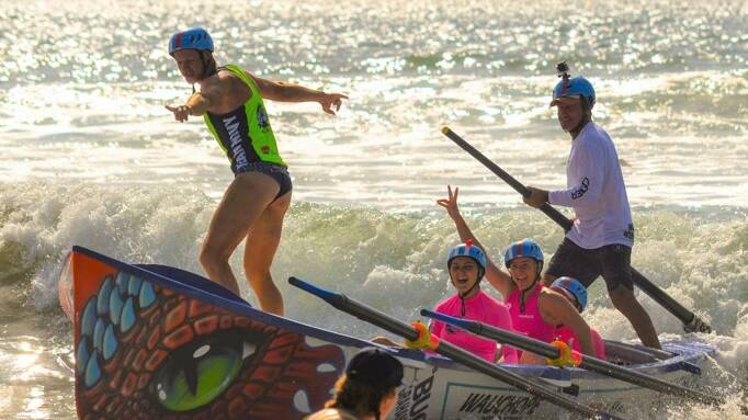 Life of the party: Ged Roods surfs the bow of the Wauchope-Bonny Hills' under-23 women's surfboat. Photo: Phil Kaufmann