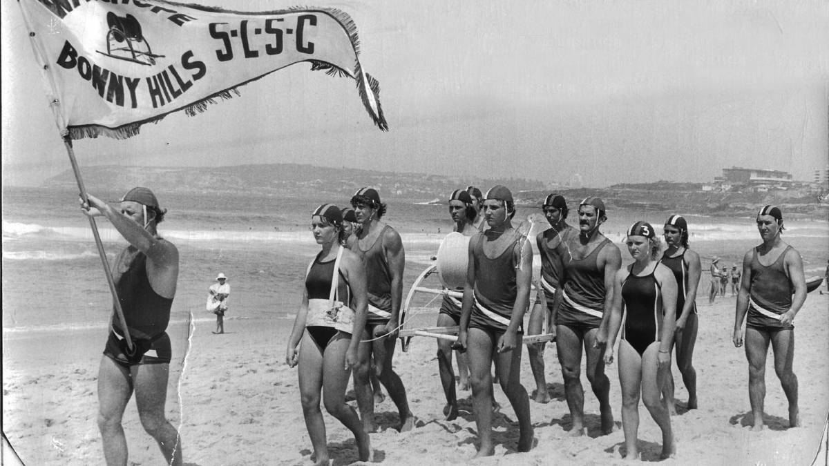 Surf lifesaving icon Robert Chalkie Bob Smith proudly carries the club standard. Daughter Leanne is behind in the belt, son Peter helps carry the reel and daughter Megan is to his left (no. 3).