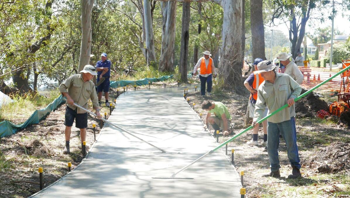 MANY HANDS MAKING LIGHT WORK: Volunteers smooth concrete on a section of the Beach to Beach Riverwalk in Dunbogan.